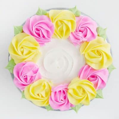 在奶油中创建简单质朴的线条，然后用粉色和黄色的奶油玫瑰花装饰!