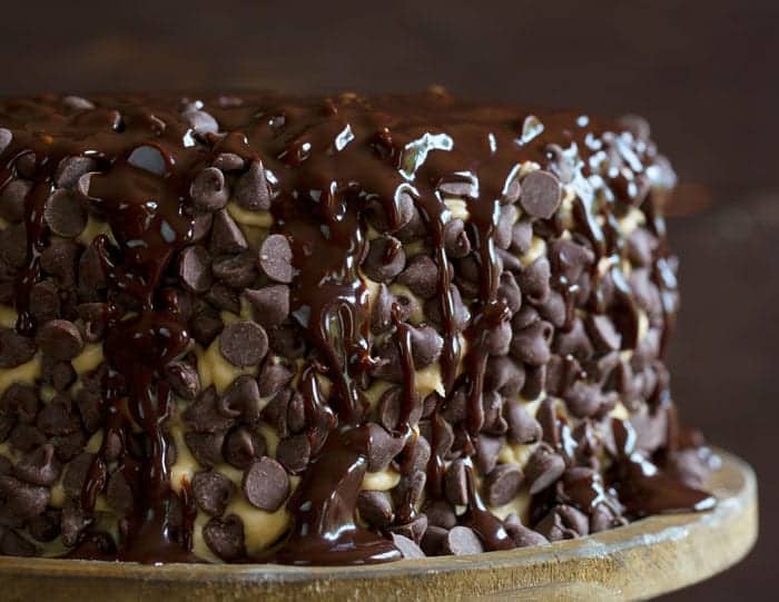 在曲奇饼面团盖与巧克力糖浆的果仁巧克力层蛋糕在一个土气木蛋糕立场滴下在上面。
