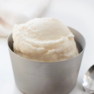 一勺软冰淇淋在白色柜台上的金属碗中，附近有汤匙。